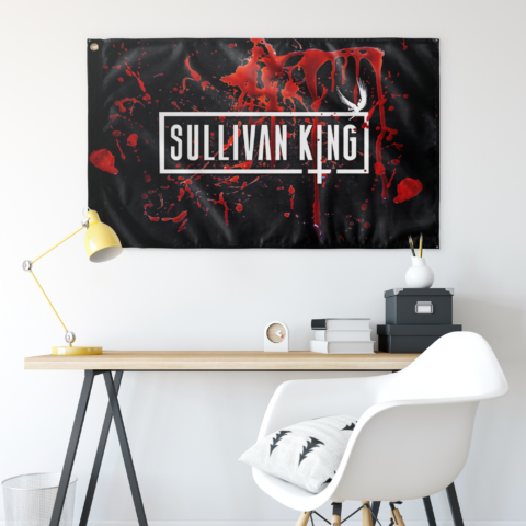 Blood splatter rave flag hung on wall above a desk with yellow lamp and chair