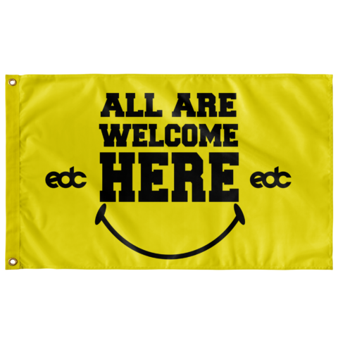 Bright yellow rave flag reading All Are Welcome Here with smiley face and EDC logos