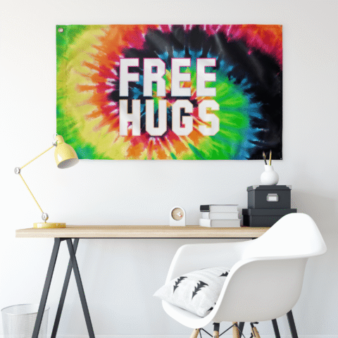 Tie dye spiral rave flag reading FREE HUGS hung on wall above a desk setup