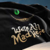 Cheshire cat grin flag waving outdoors against blue sky with We're All Mad Here script