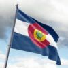 Colorado state rave flag with cannabis leaf mascot waving on pole against cloudy sky