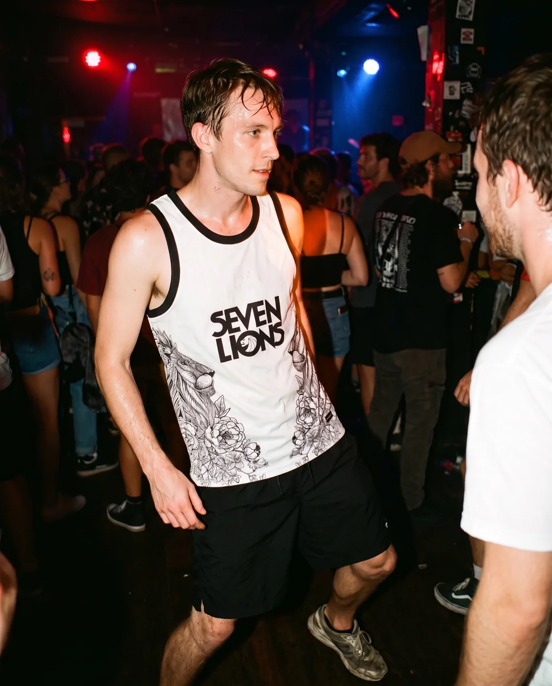 Man wearing a white graphic basketball jersey over a tank at an indoor rave