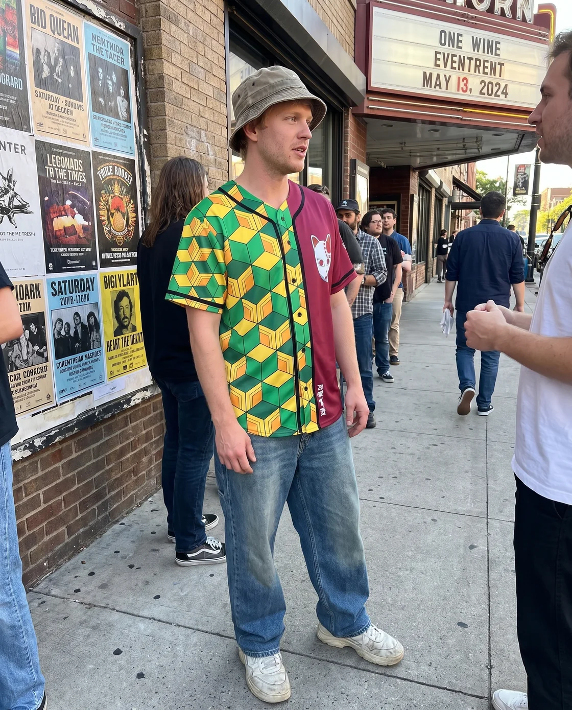 Man styling a green and yellow baseball jersey with wide jeans and a bucket hat