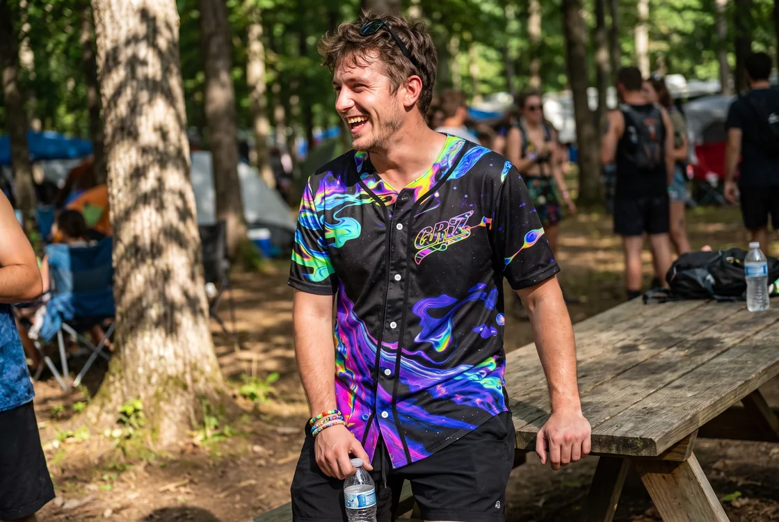 Man wearing a black GRiZ psychedelic baseball jersey open over a tee and shorts