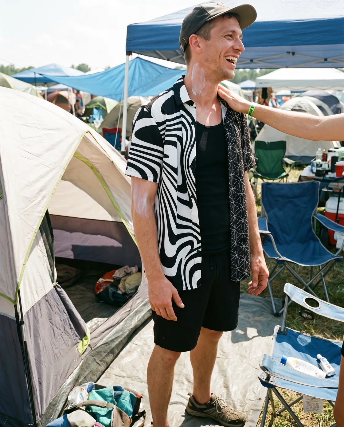 Man wearing a printed button-down shirt over a tank with shorts at a day festival