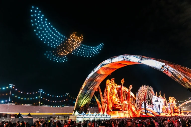 Night crowd beneath an illuminated EDC stage and owl-shaped drone display