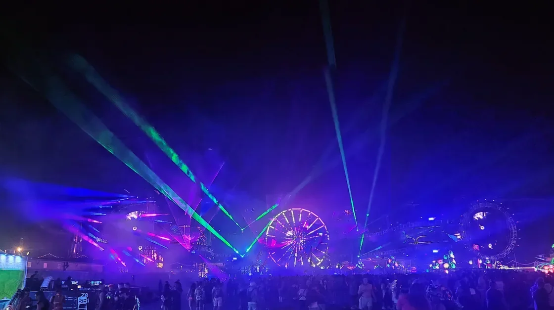 Carnival rides and a Ferris wheel glowing above an EDC crowd at night
