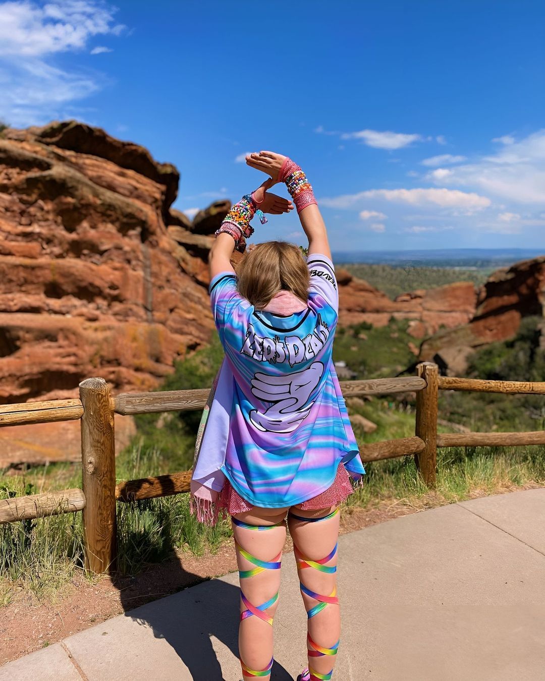 A girl in a colorful shirt jersey standing in front of a mountain.