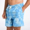 Cloud-like blue tie-dye swim trunks with side pockets and white festival emblem, close-up front view