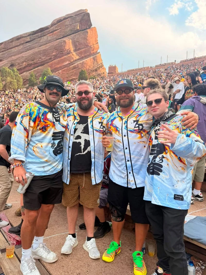 Four customers wearing matching light-blue, multicolor hockey and baseball jerseys at an outdoor concert.
