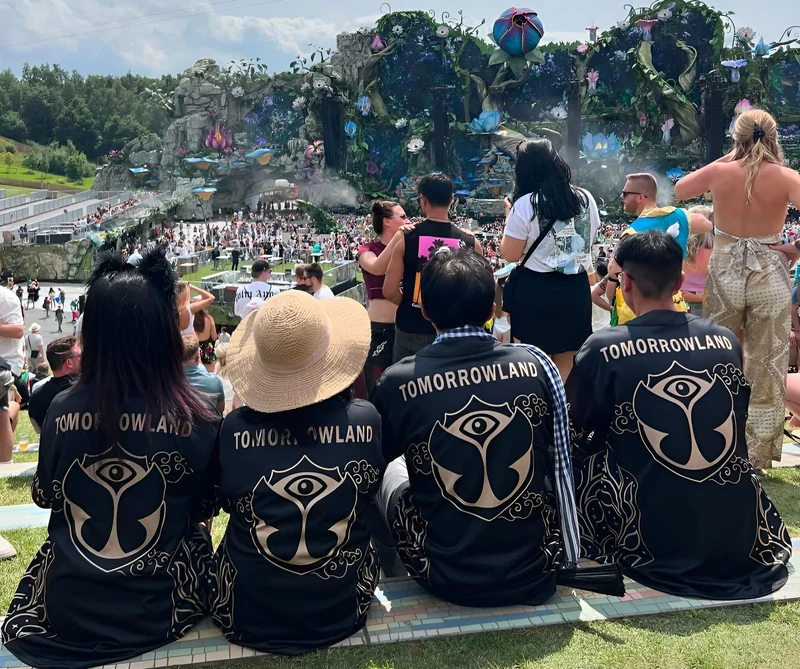 Four customers seen from behind in matching black-and-gold Tomorrowland jerseys, watching the festival stage.