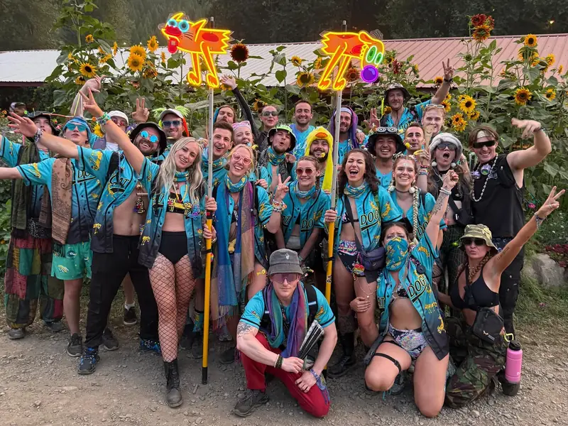 Big crew of festival friends in matching turquoise custom jerseys, holding two glowing totems.