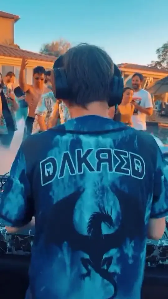 DJ wearing a blue tie-dye dragon jersey behind the decks